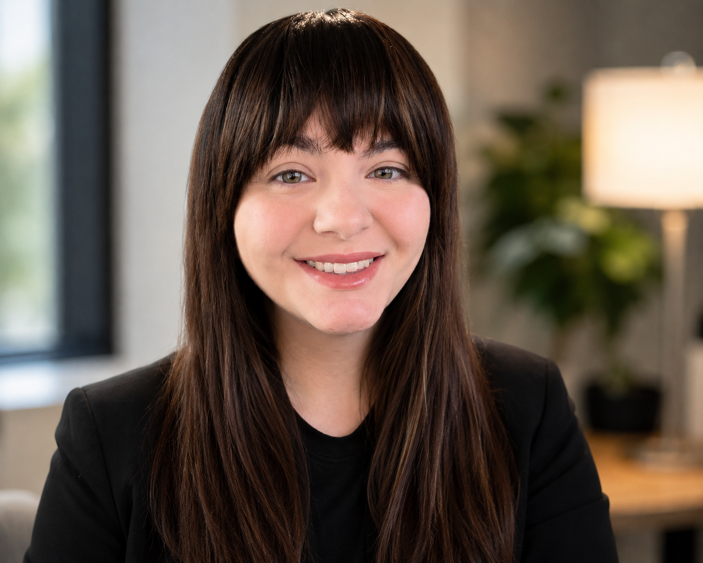 A woman with long brown hair and a black blazer smiling in a well-lit indoor setting.