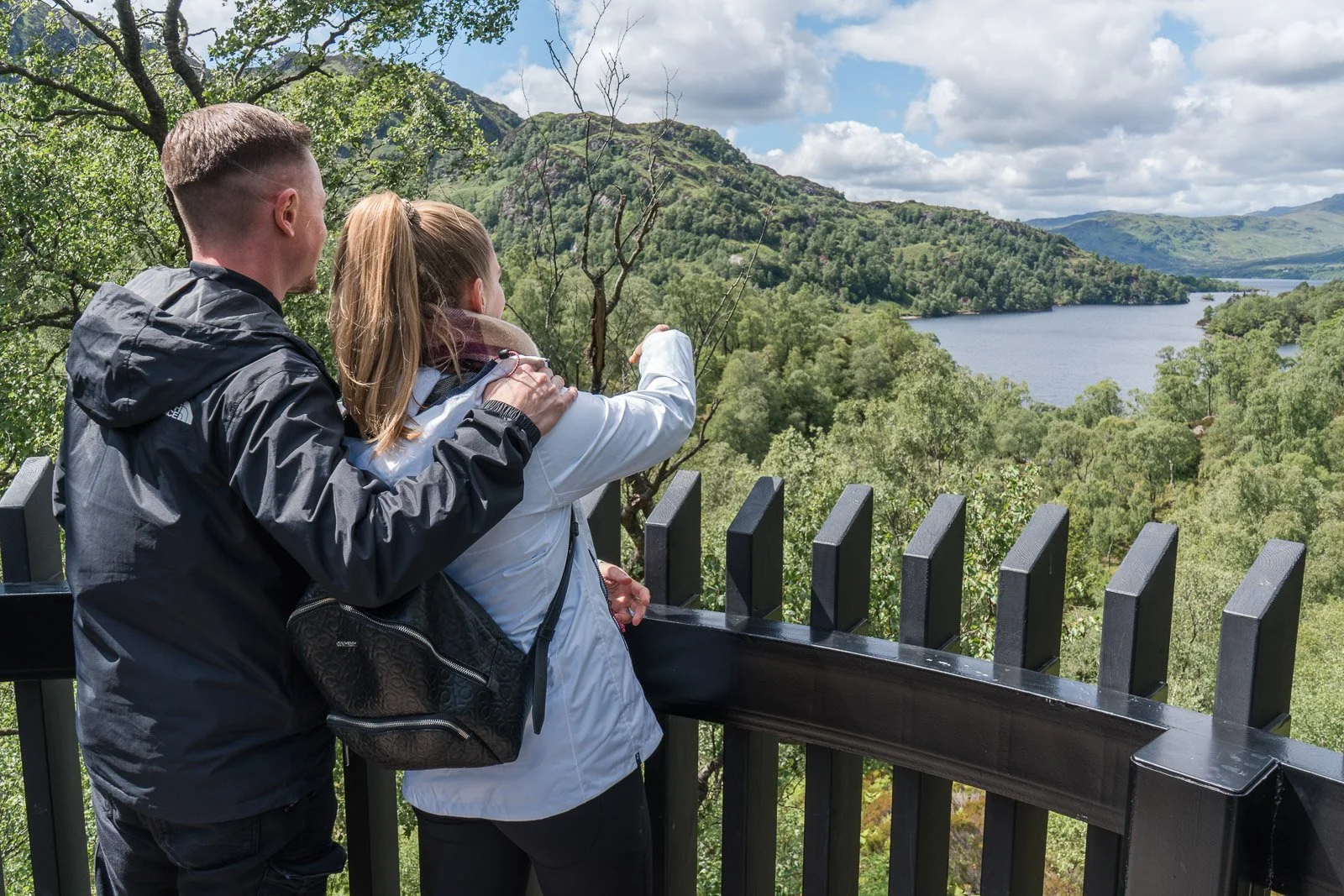 Loch Katrine viewing platform overlooking a lush green valley with a winding river and mountains in the distance, with cloudy sky.