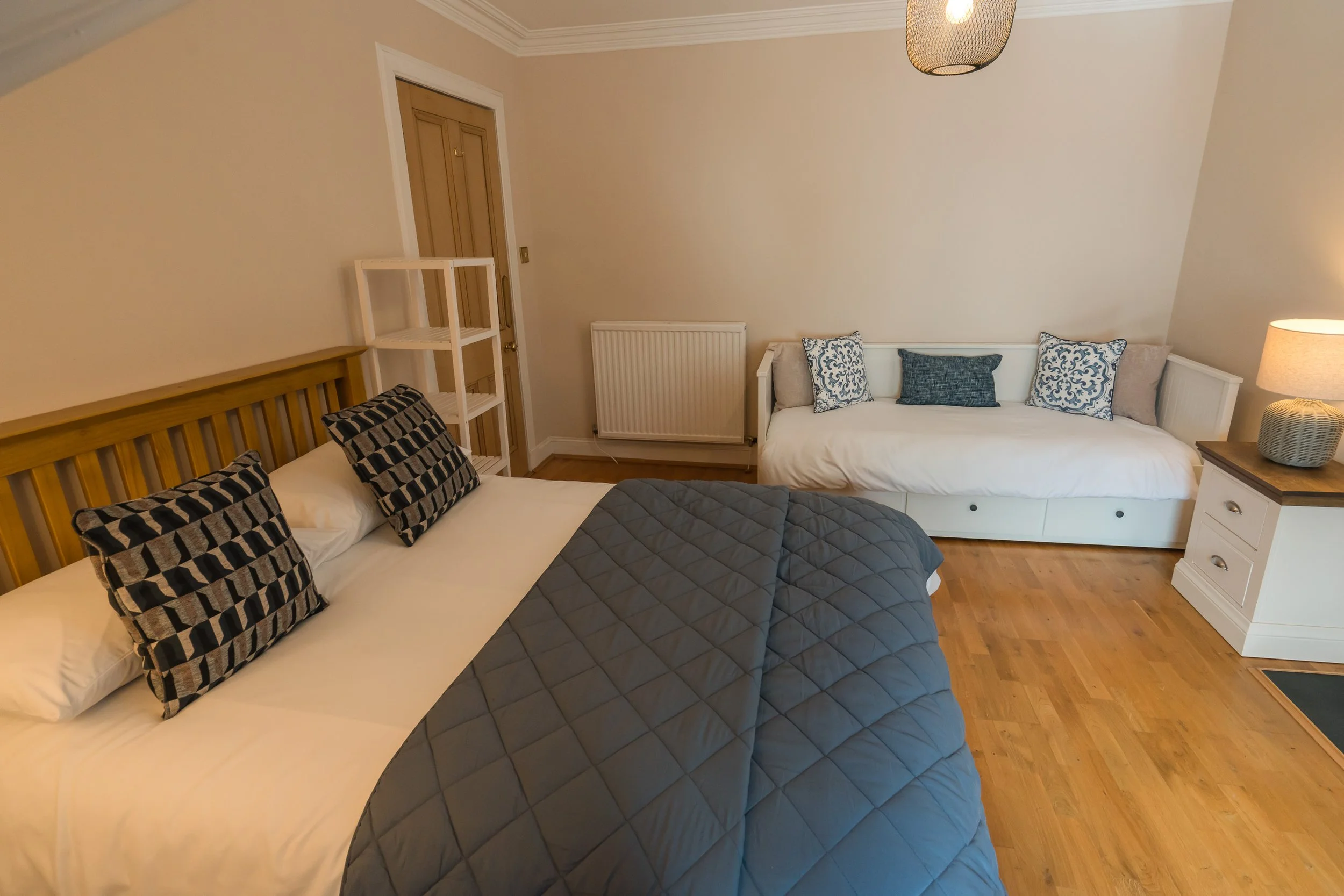 A bedroom with a bed, couch, pillows, lamp, and wooden flooring.