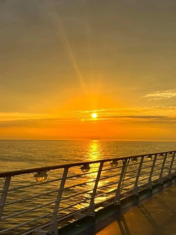 Sunset over the ocean viewed from a ship's deck with railing.
