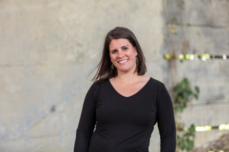 Michelle standing outdoors in front of a textured wall with some greenery.