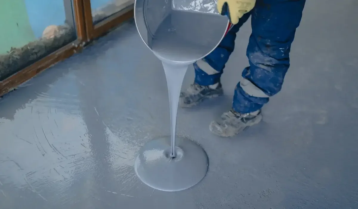 Worker pouring gray epoxy coating onto a prepared concrete floor to create a smooth, durable surface.