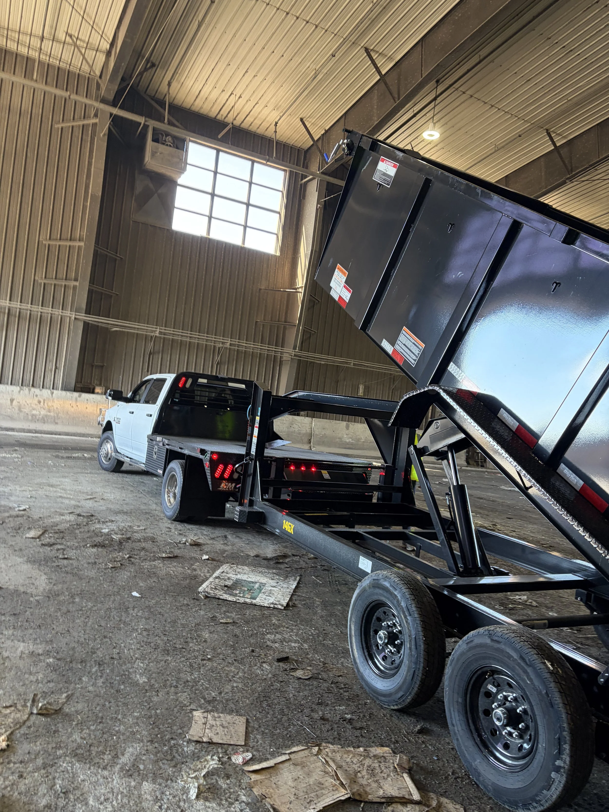 A pick up truck with a dump trailer extending and unloading trash within a waste disposal facility 