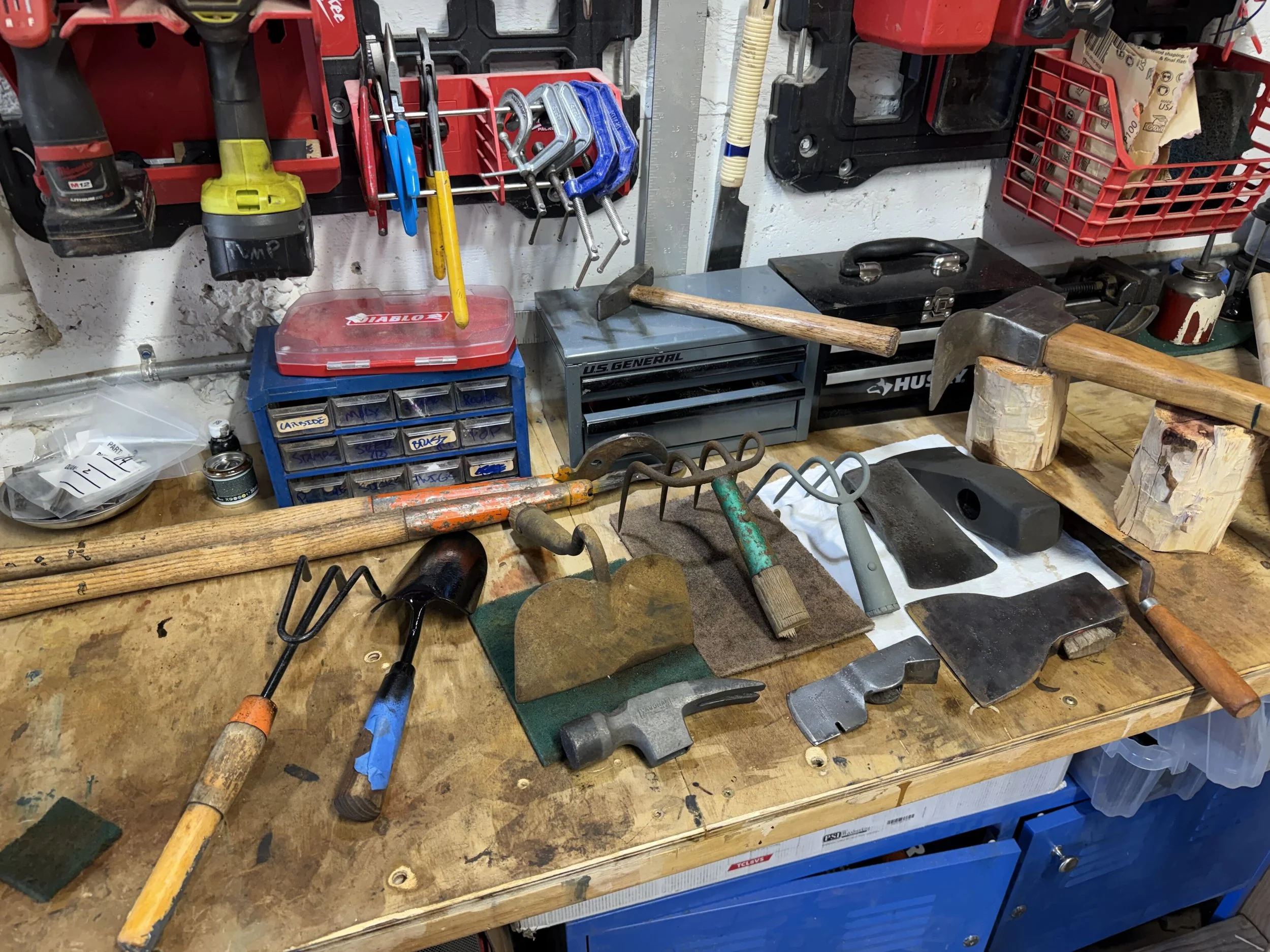 A cluttered workbench with tools such as hammers, clamps, a drill, and various small parts organized in containers.