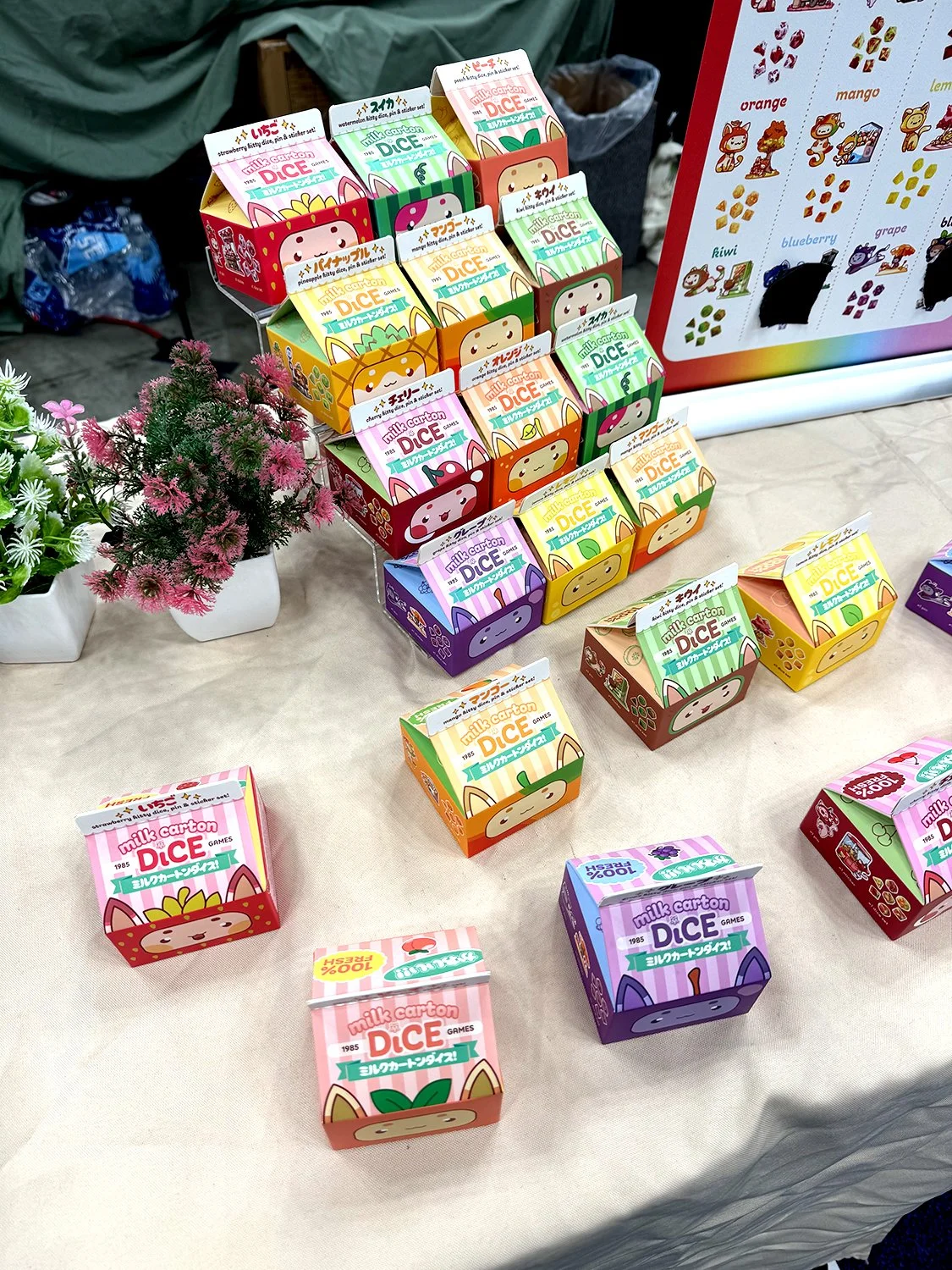 Photo of a booth display at Gen Con with dice containers shaped like milk cartons depicting cute cate faces.