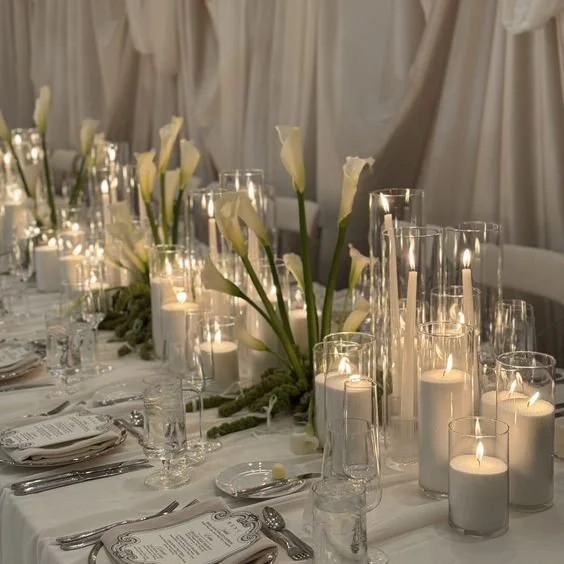 Elegant table setting at a formal event with white flowers and various lit candles in glass holders.