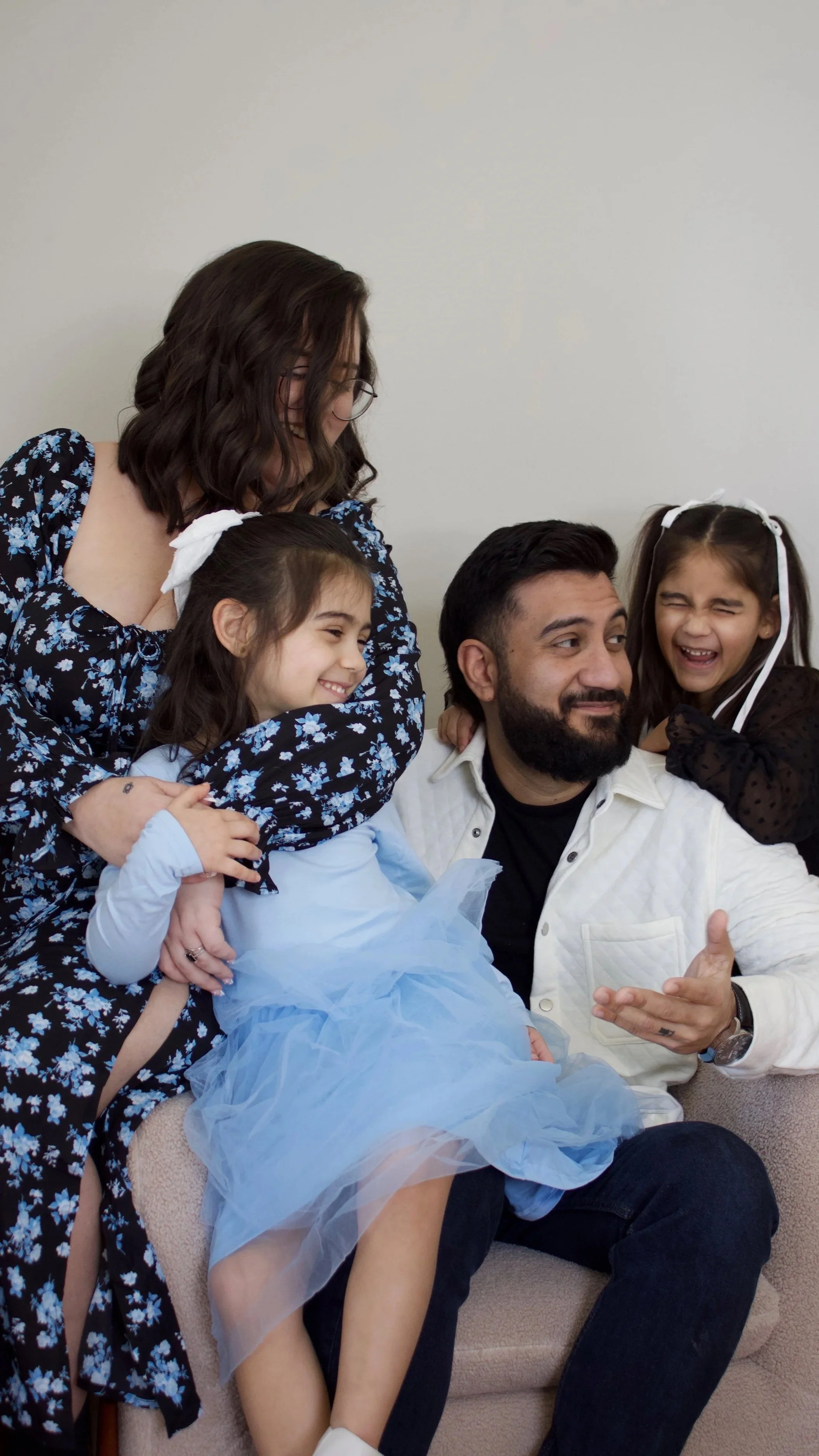 A family of five showing affection and happiness together, sitting on a light-colored couch with a plain background.