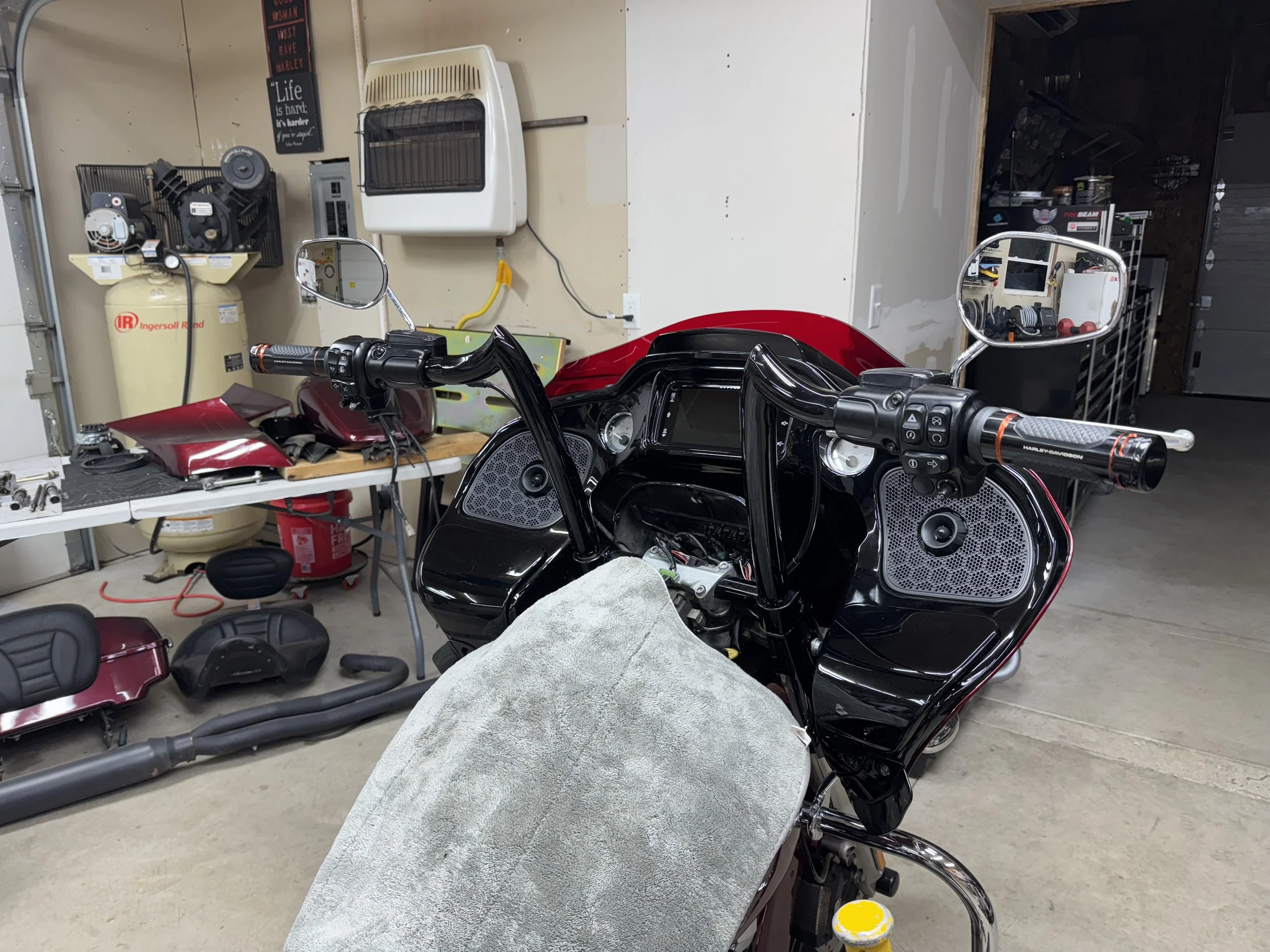 A motorcycle in a garage or workshop with various tools and equipment. There are handles, mirrors, and parts of the motorcycle visible, along with workbenches and storage shelves in the background.