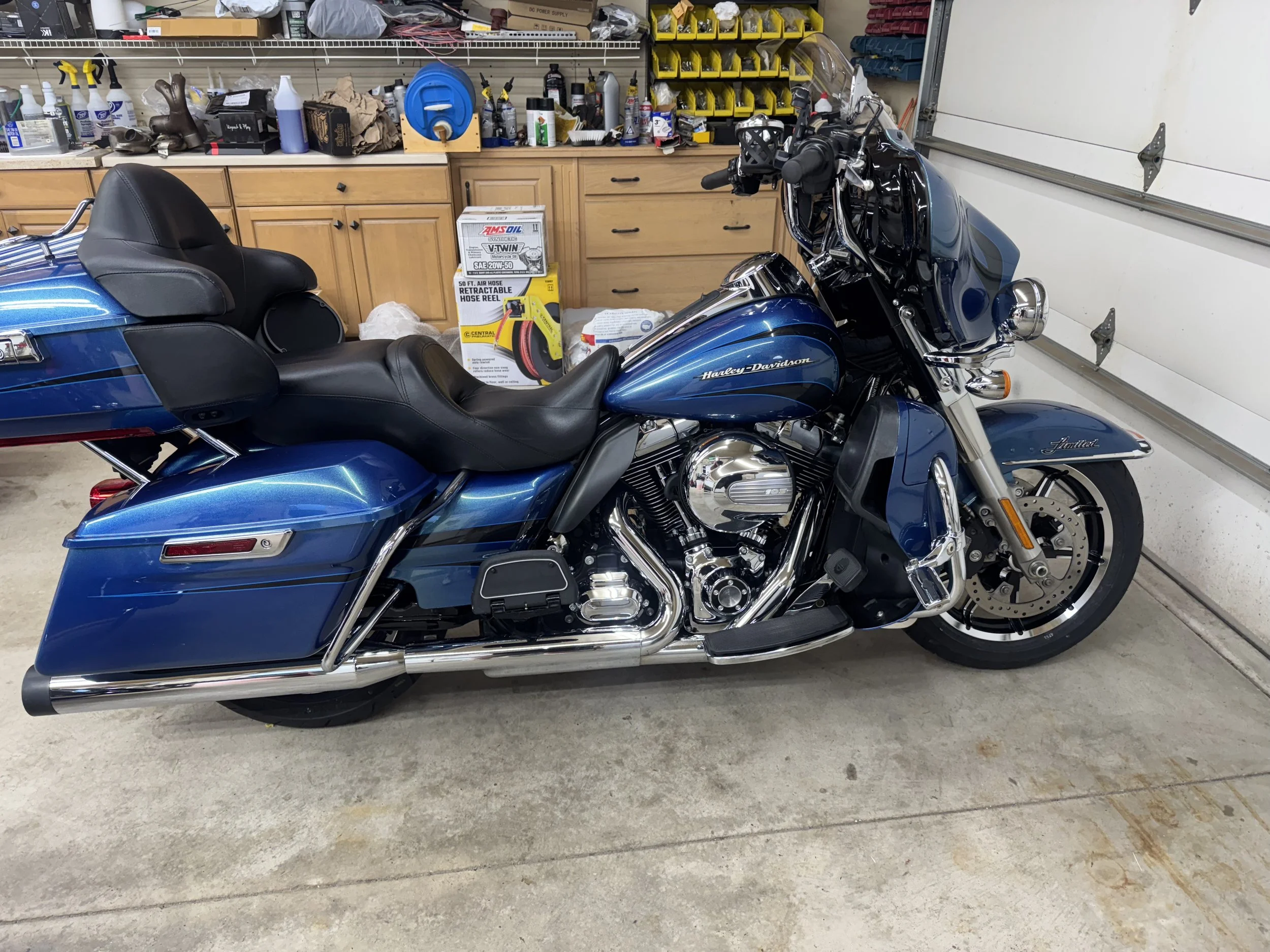 A blue Harley Davidson motorcycle parked in a garage with a workbench and various tools and supplies behind it.