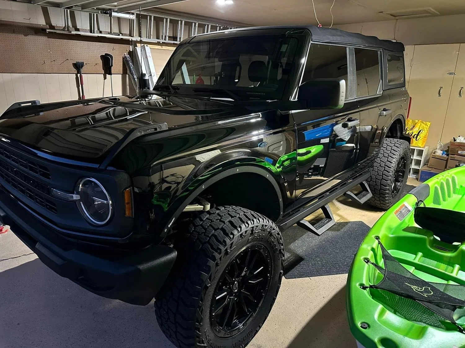 A black off-road vehicle with large tires parked in a garage, with a green kayak nearby.