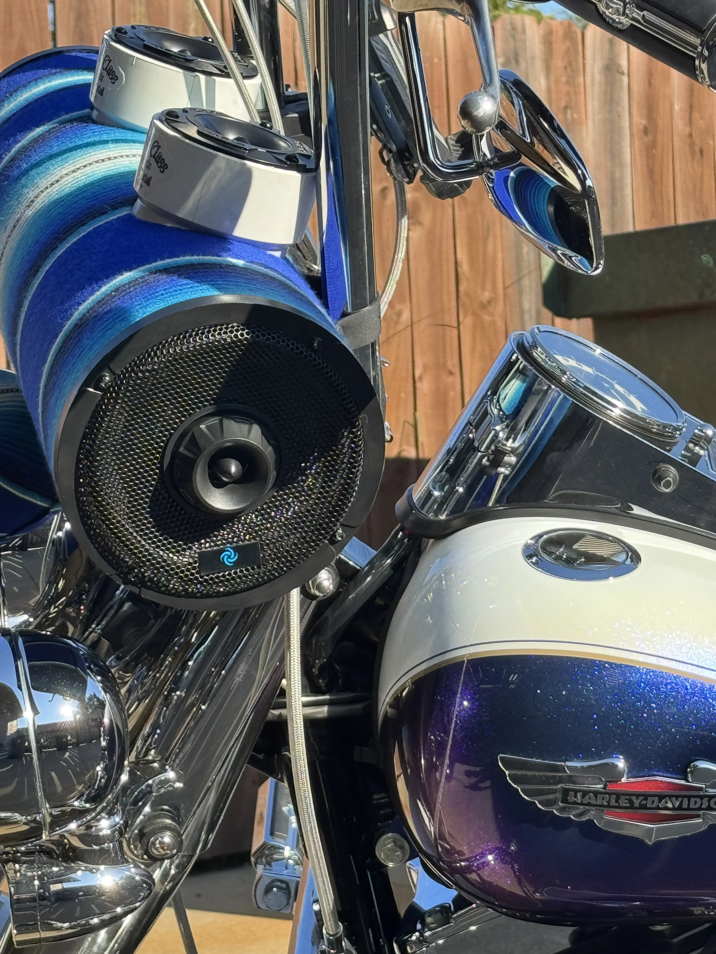 Close-up view of a Harley-Davidson motorcycle with a blue and black color scheme, featuring chrome details, a fuel tank with the Harley-Davidson logo, and blue and white striped hat boxes attached to the front.