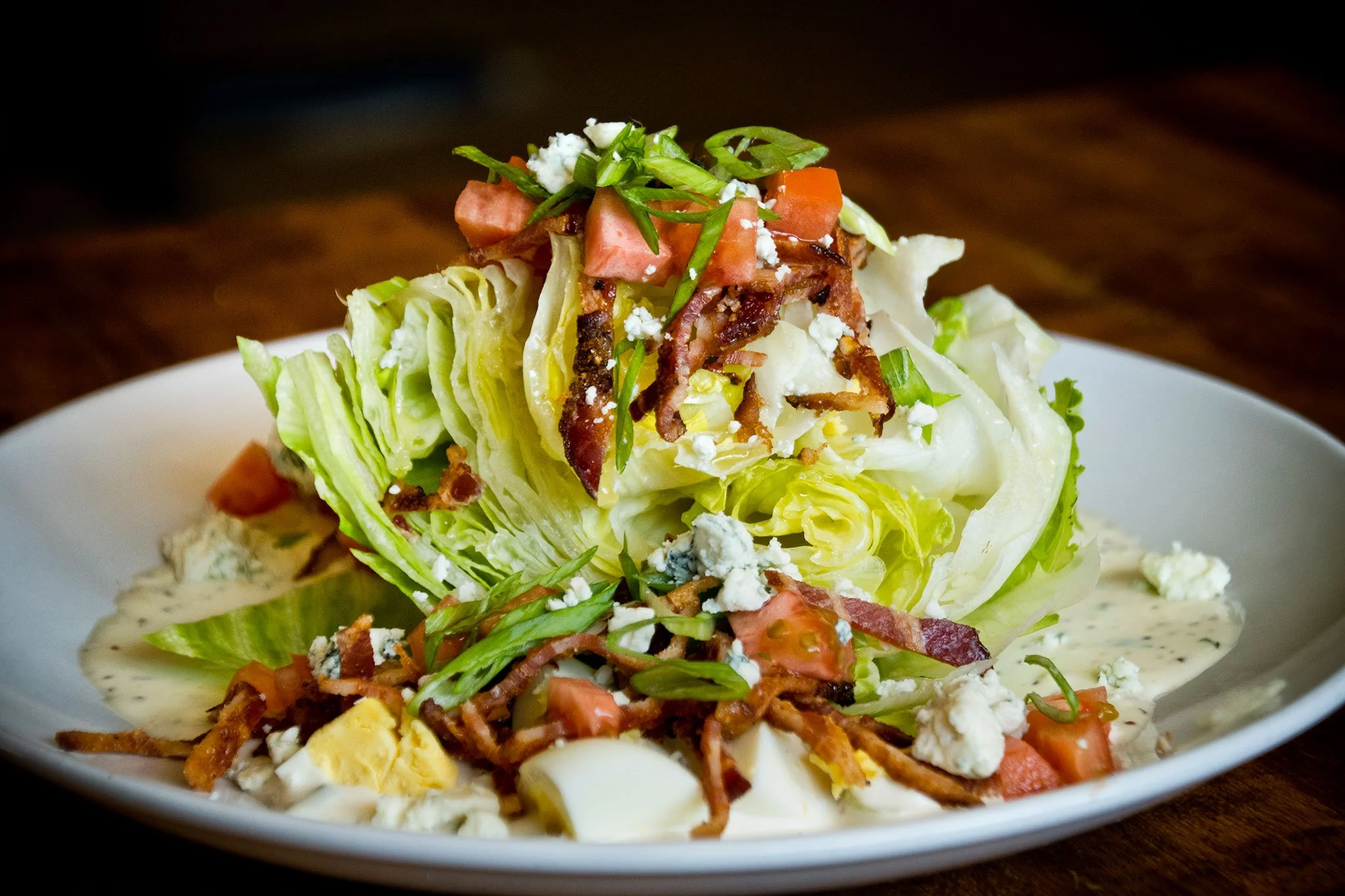 A plate of salad with lettuce, tomato, bacon, blue cheese, green onions, and sliced hard-boiled egg.