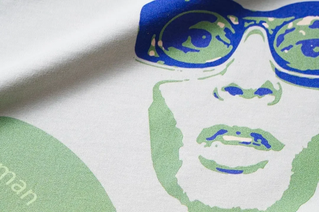 Close-up of a white fabric with a printed design of a person's face wearing sunglasses in green and blue colors.