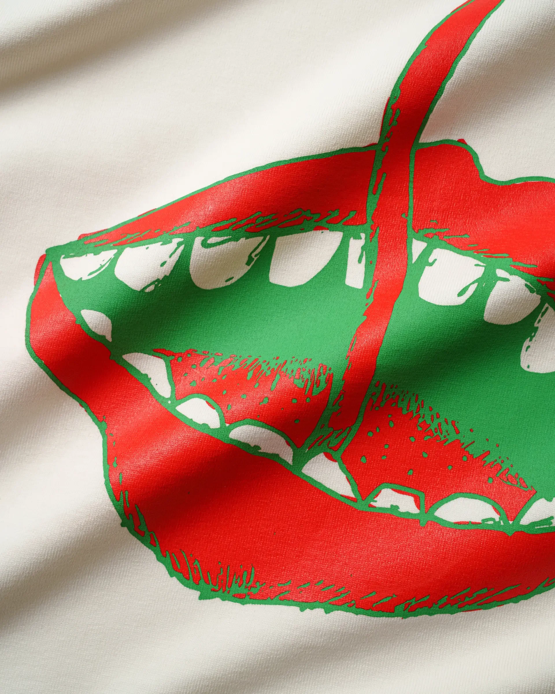 A printed graphic on fabric featuring a red and green design resembling a stylized bicycle helmet and goggles, with curved shapes and lines.
