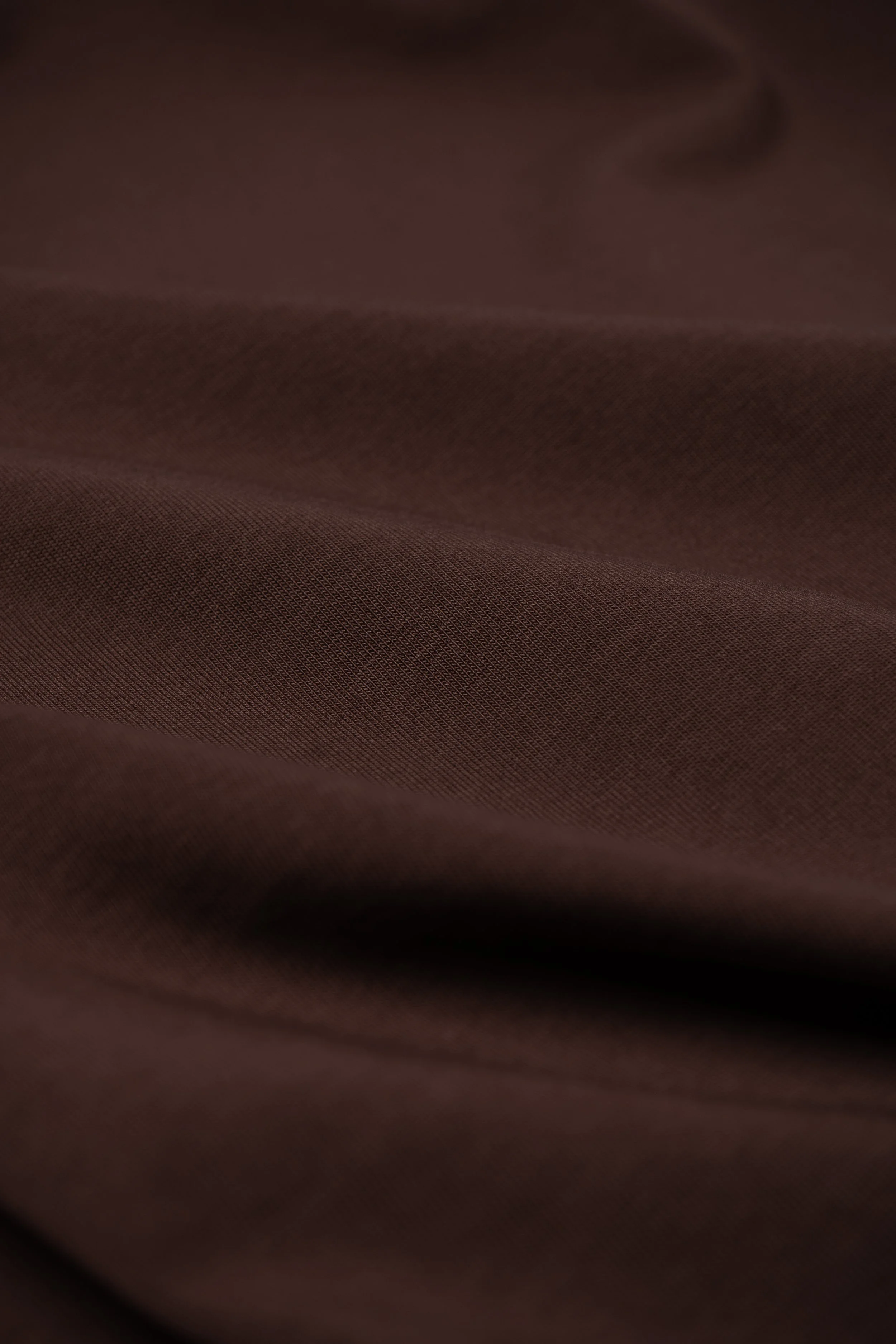 Close-up view of dark brown, textured fabric with smooth, wavy folds.