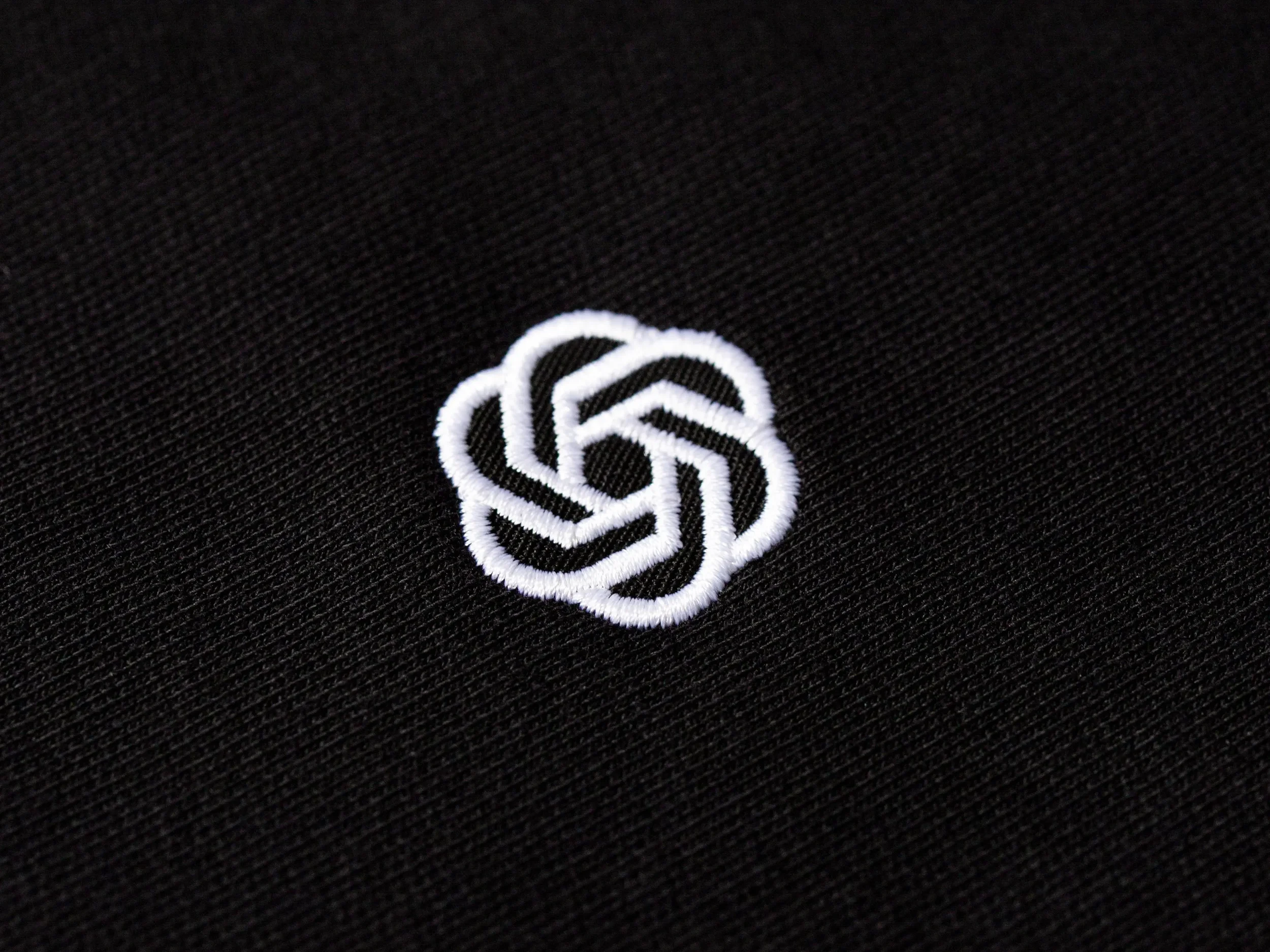 Close-up of embroidered white logo on black fabric.