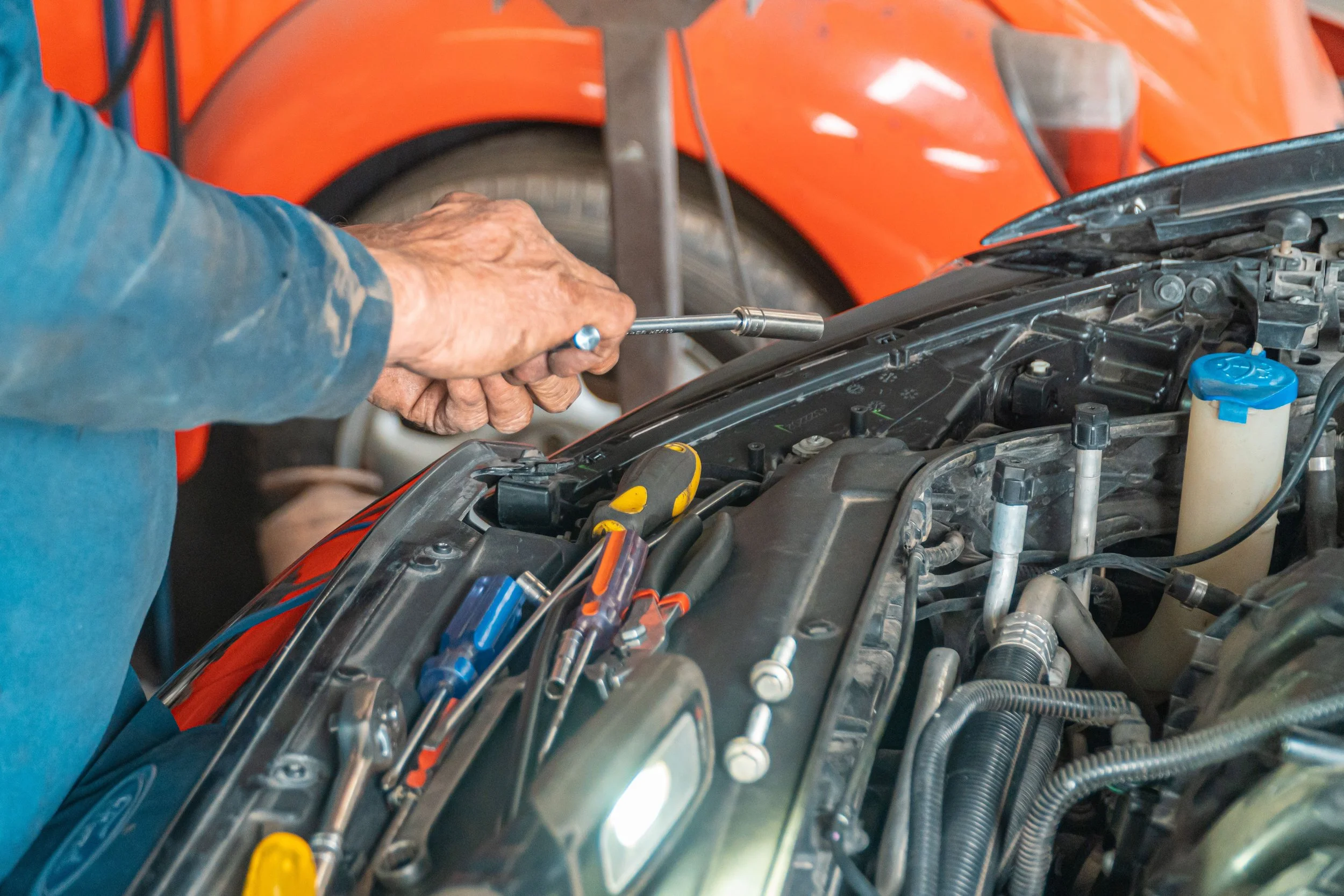 A mechanic holds a socket wrench above a car engine with tools nearby.