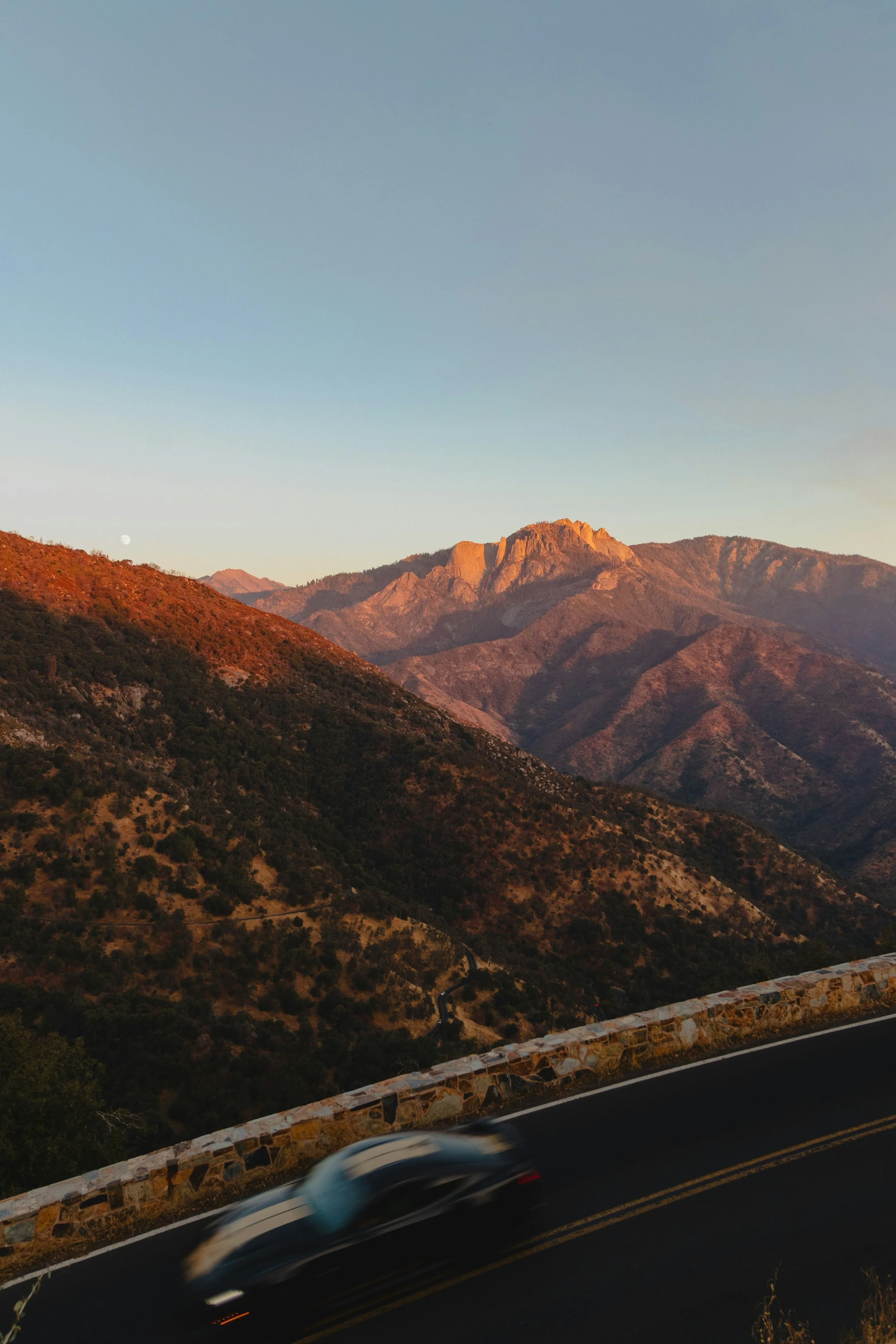 A car traveling on a mountain road at sunset.