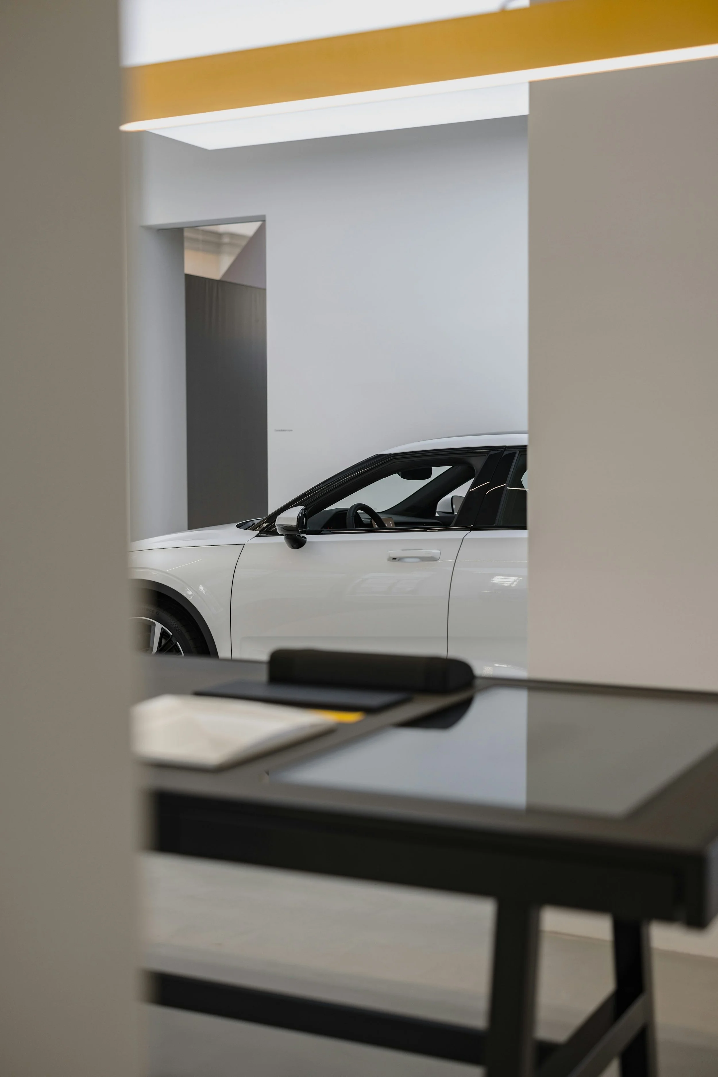 White car displayed behind a desk in a bright dealership showroom.
