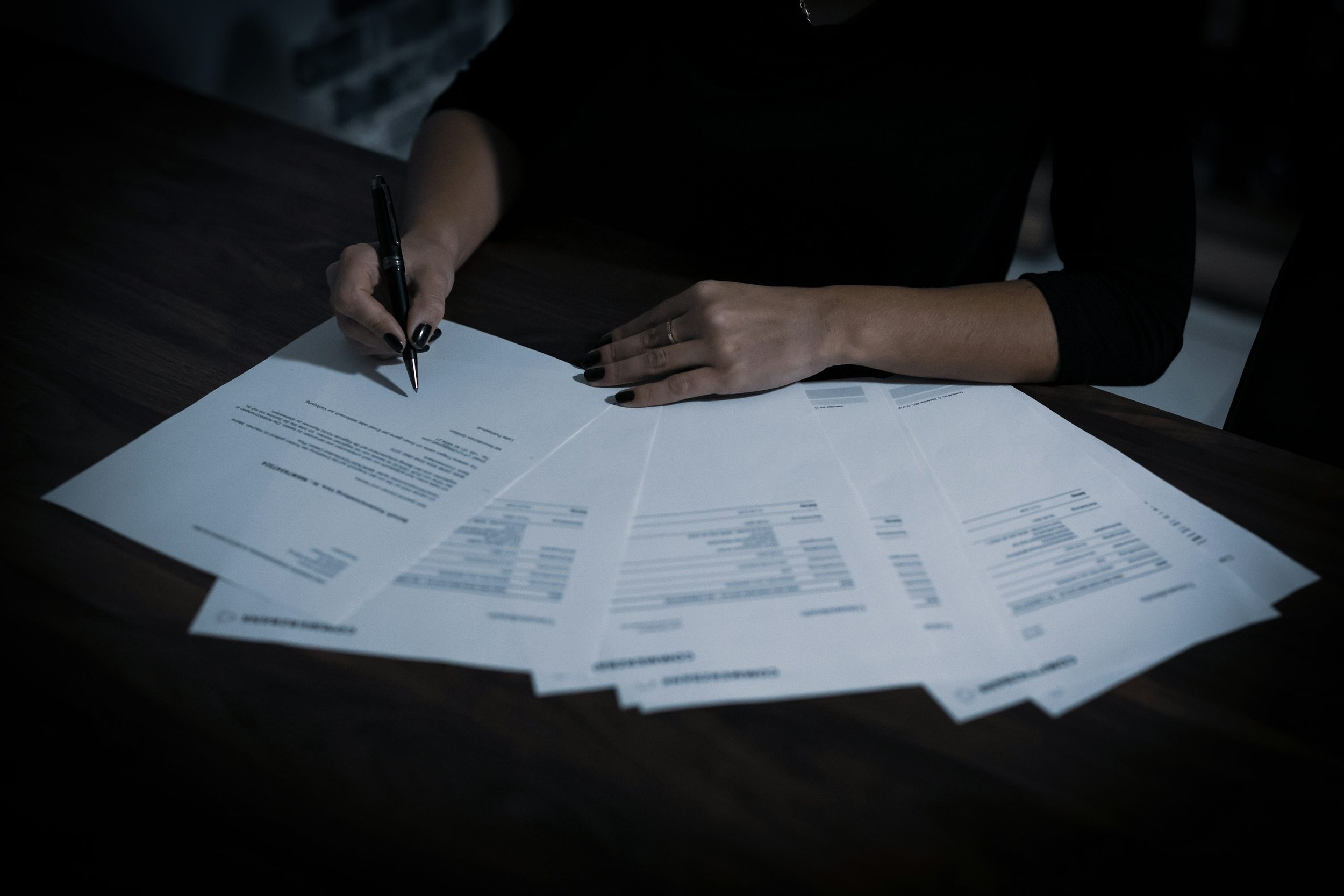 Hands holding a pen while reviewing documents spread across a desk.