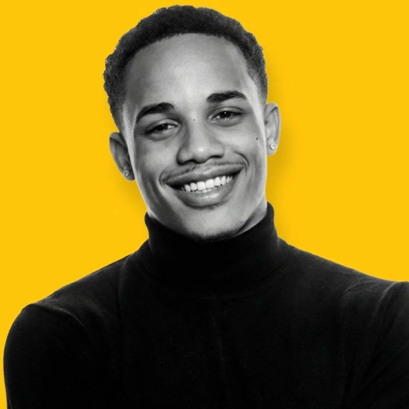 A black and white portrait of a smiling young person with short hair, wearing a black turtleneck, against a bright yellow background.