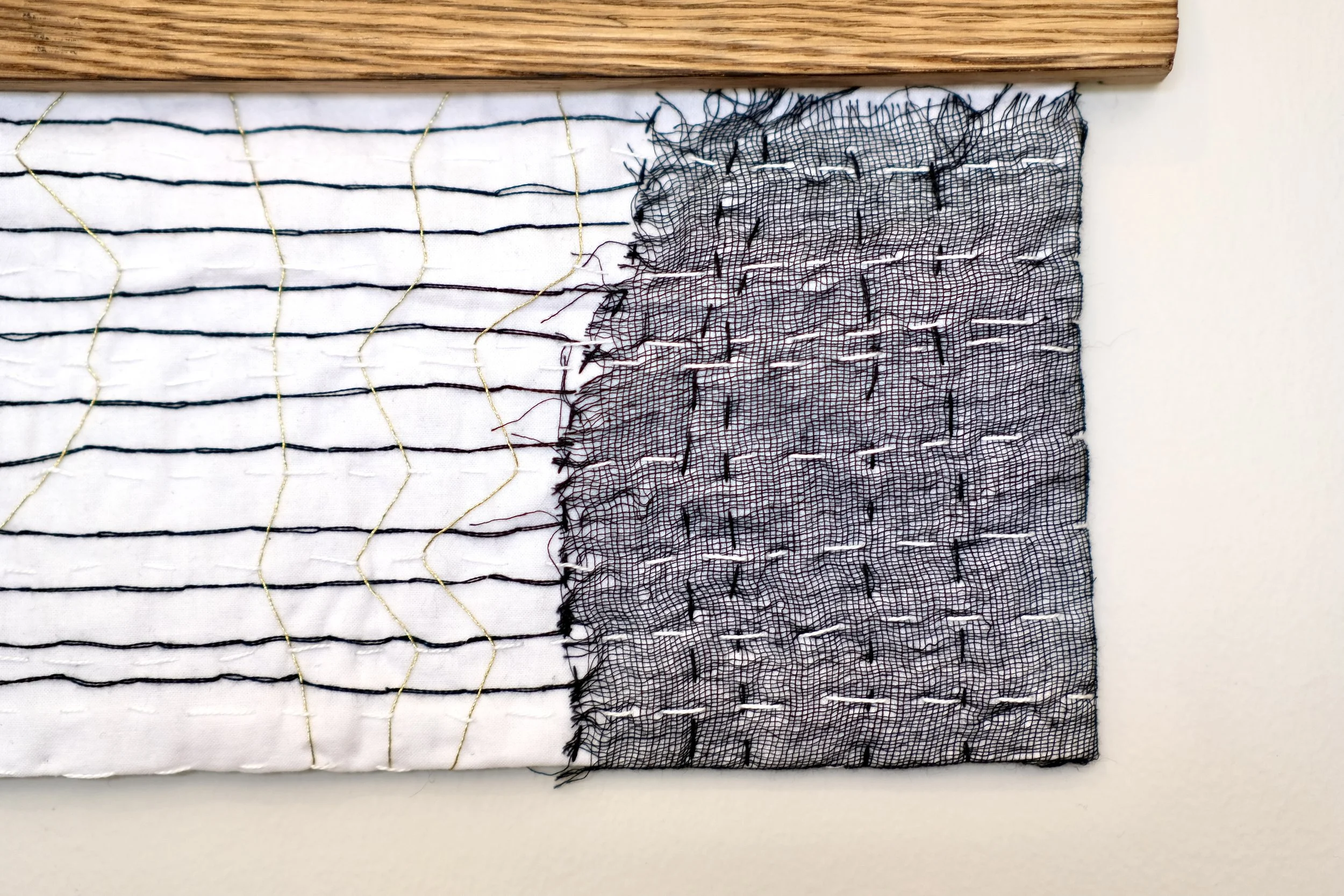 Layer pieces of black and gold embroidered fabric hanging with by a reclaimed, wood fired oak or pine hanger.