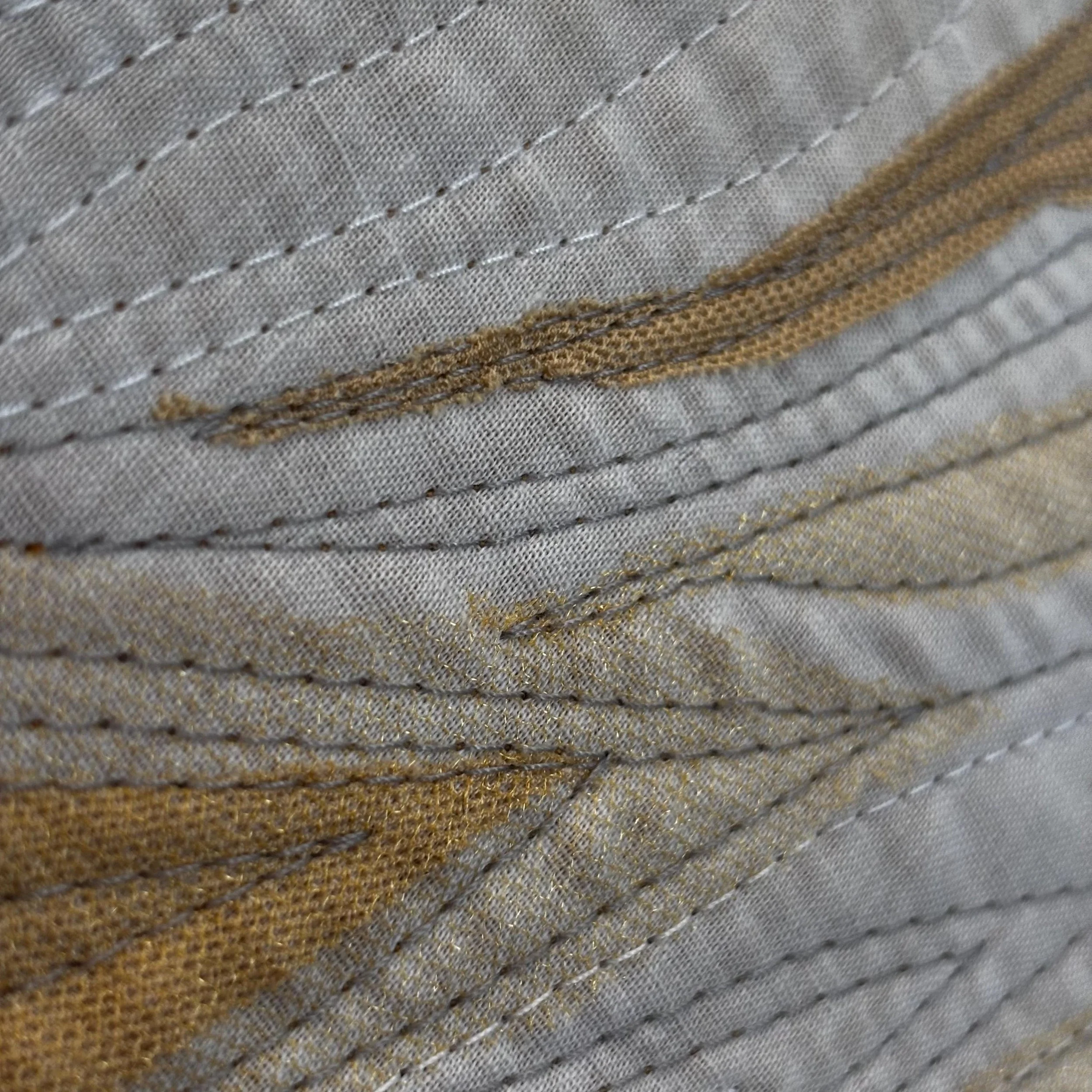 Close-up of fabric with detailed stitching and a strip of brown leather or suede material.