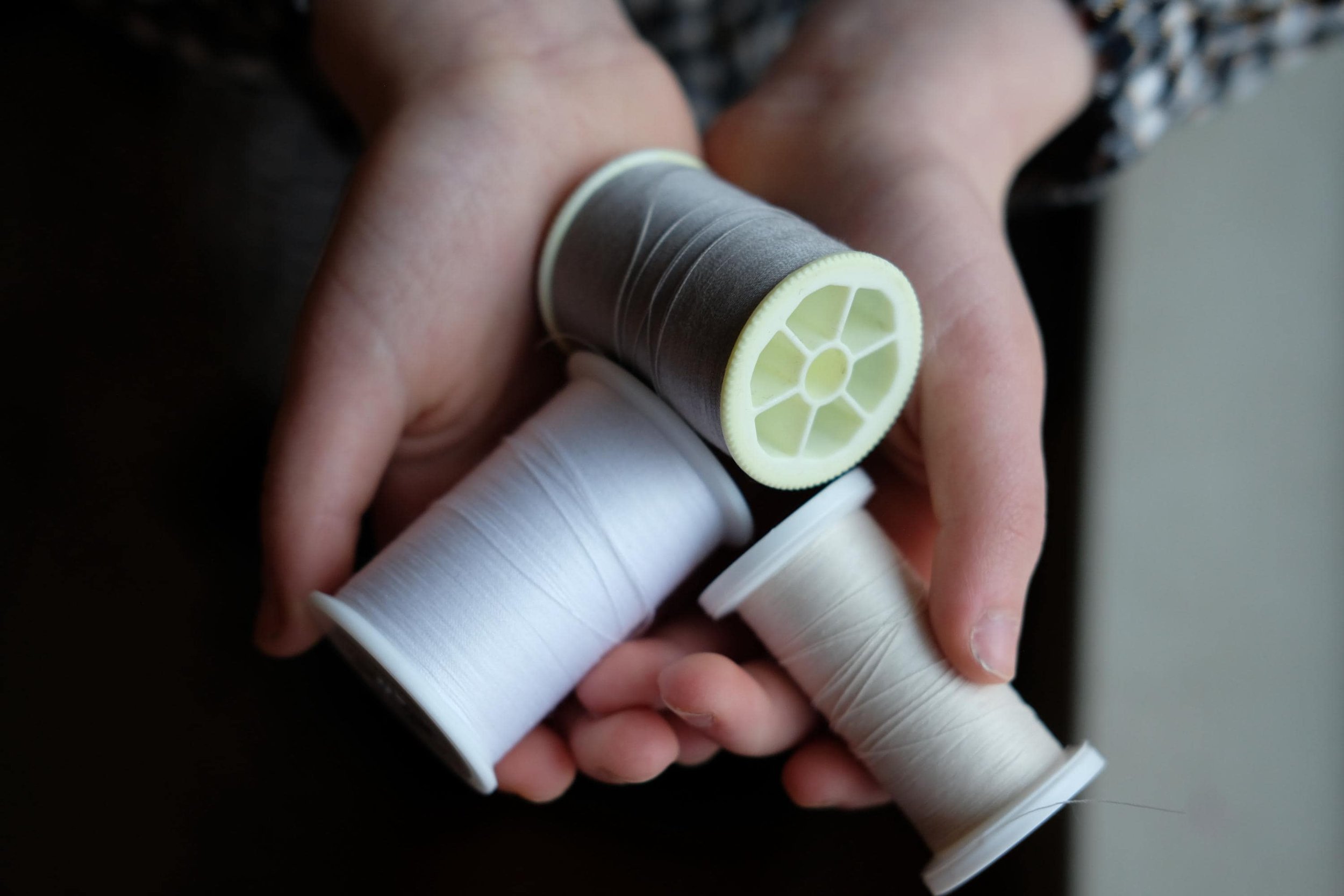 Close-up of a person's hand holding several vintage and modern thread bobbins.