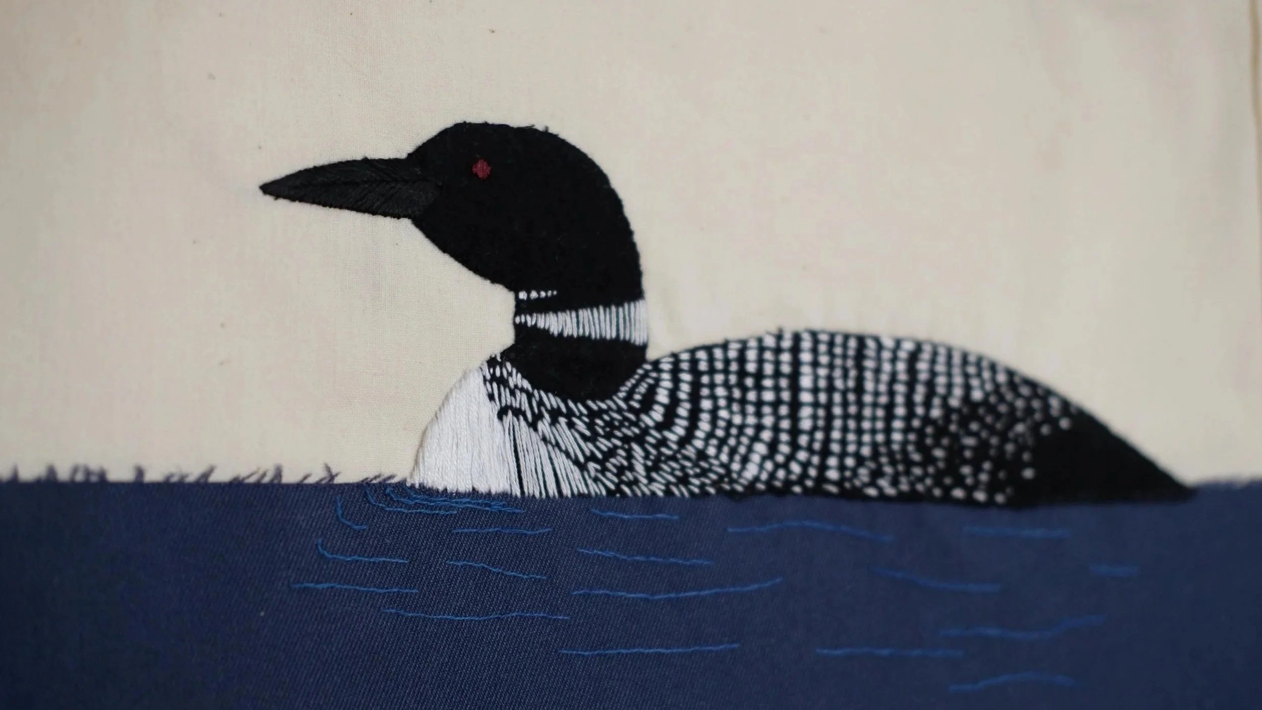 Hand-stitched and Embroidered of the common loon bird, on fabric with a white background and blue and black details.