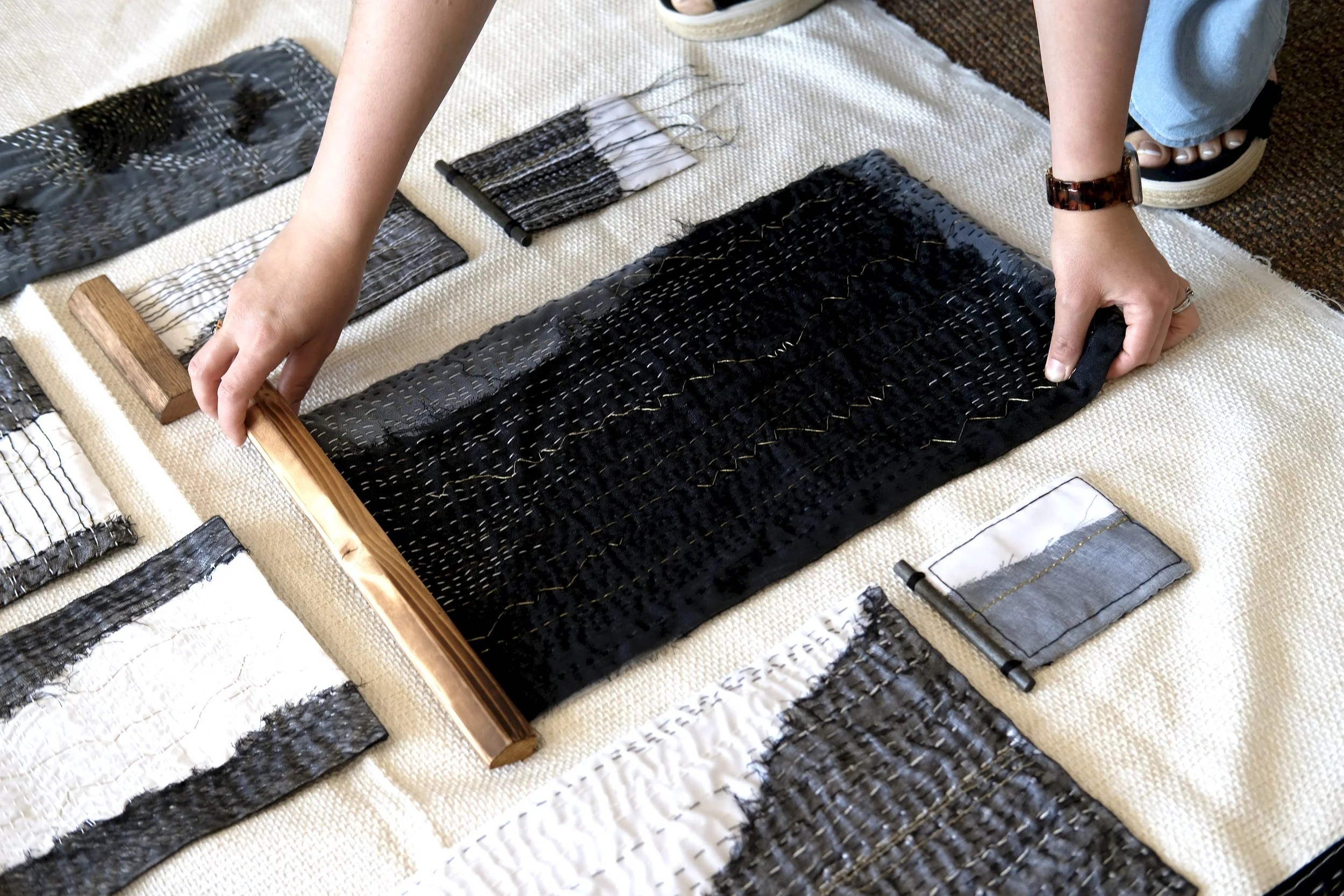Person bending over, working with fabric swatches on a beige textured surface, with black, white, and gray patterns.