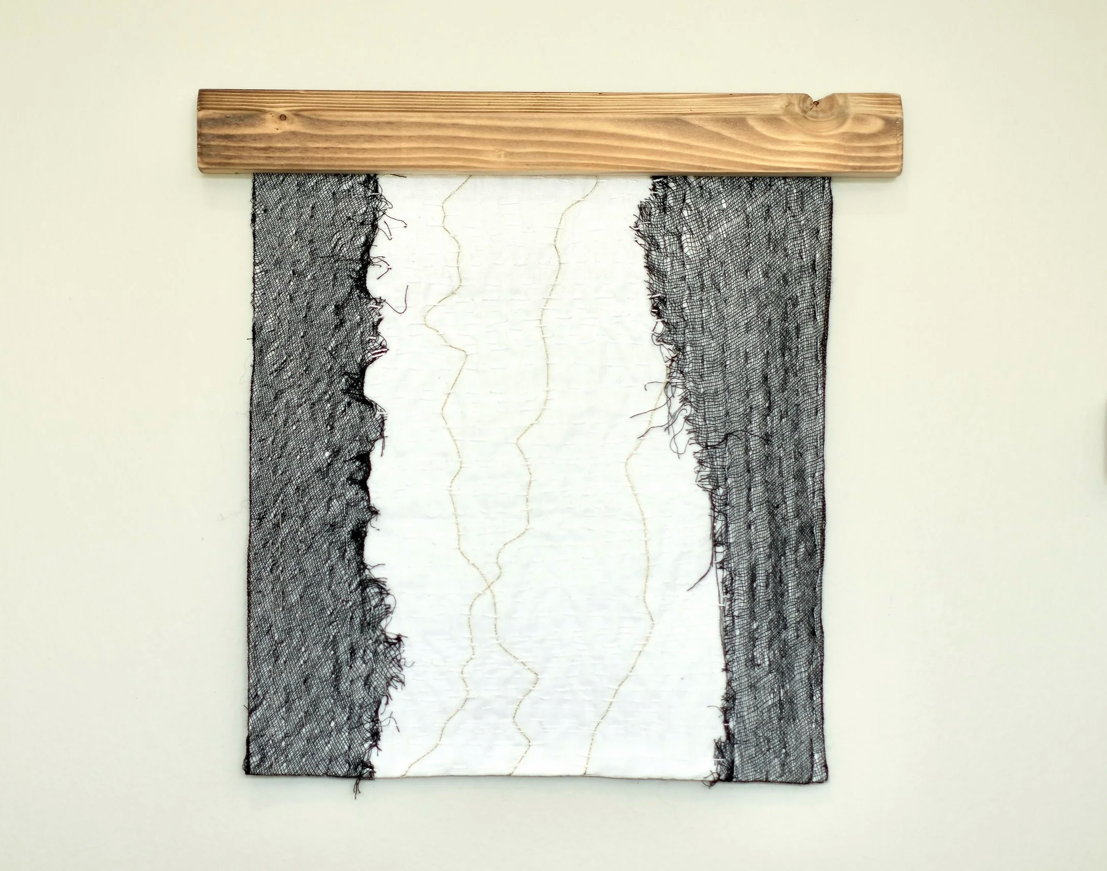Textile piece featuring a central white fabric with yellow zigzag stitching, flanked by black netting on both sides, mounted on a wooden board.