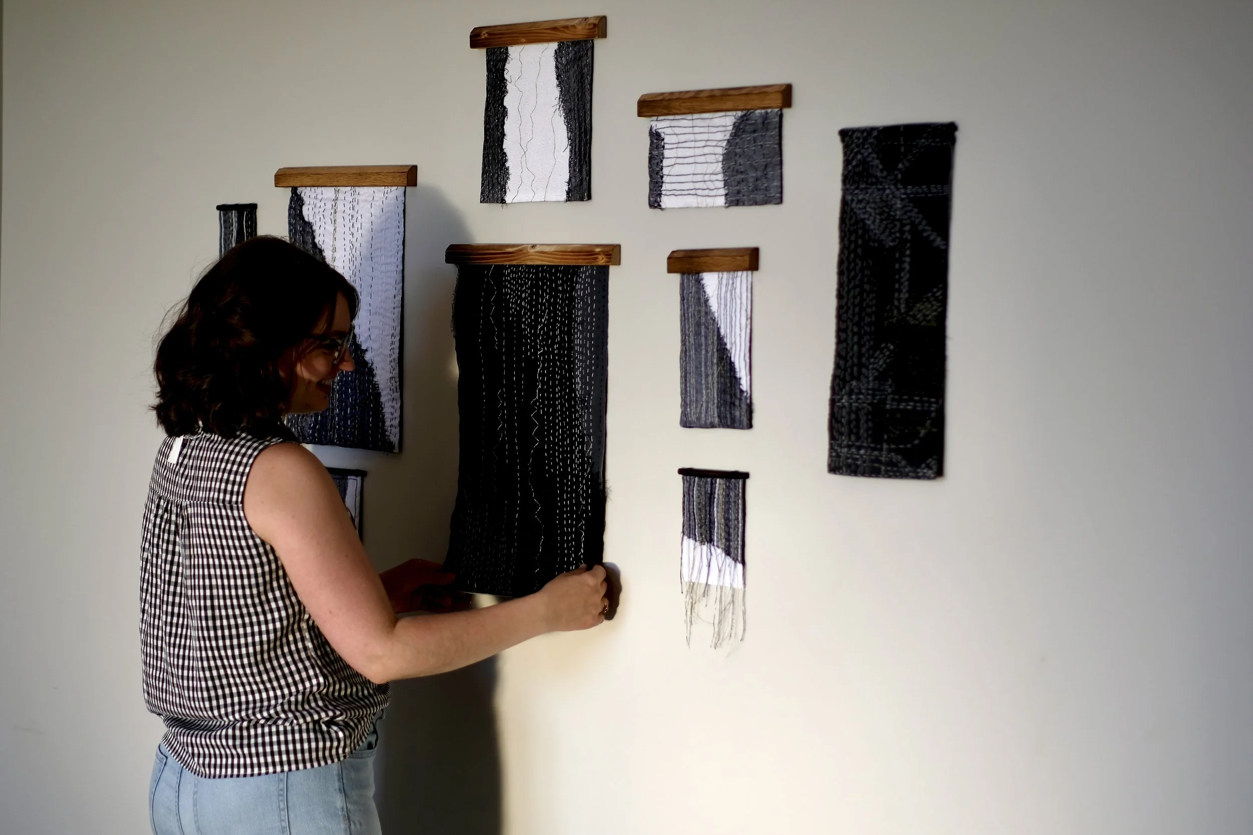 Artist Sarah Kirby of Larch Street Studio arranging black and white textile art pieces on a white wall.