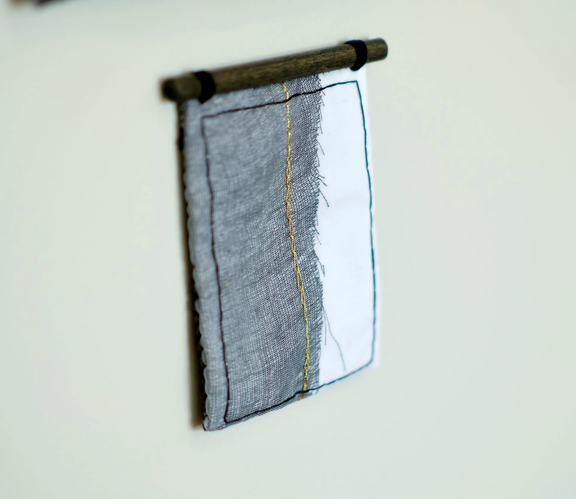 Close-up of a piece of fabric with embroidered edges hanging from a wooden dowel on a white wall.