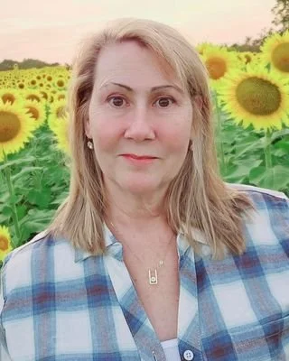 A woman with blonde hair takes a selfie in a sunflower field during daytime.