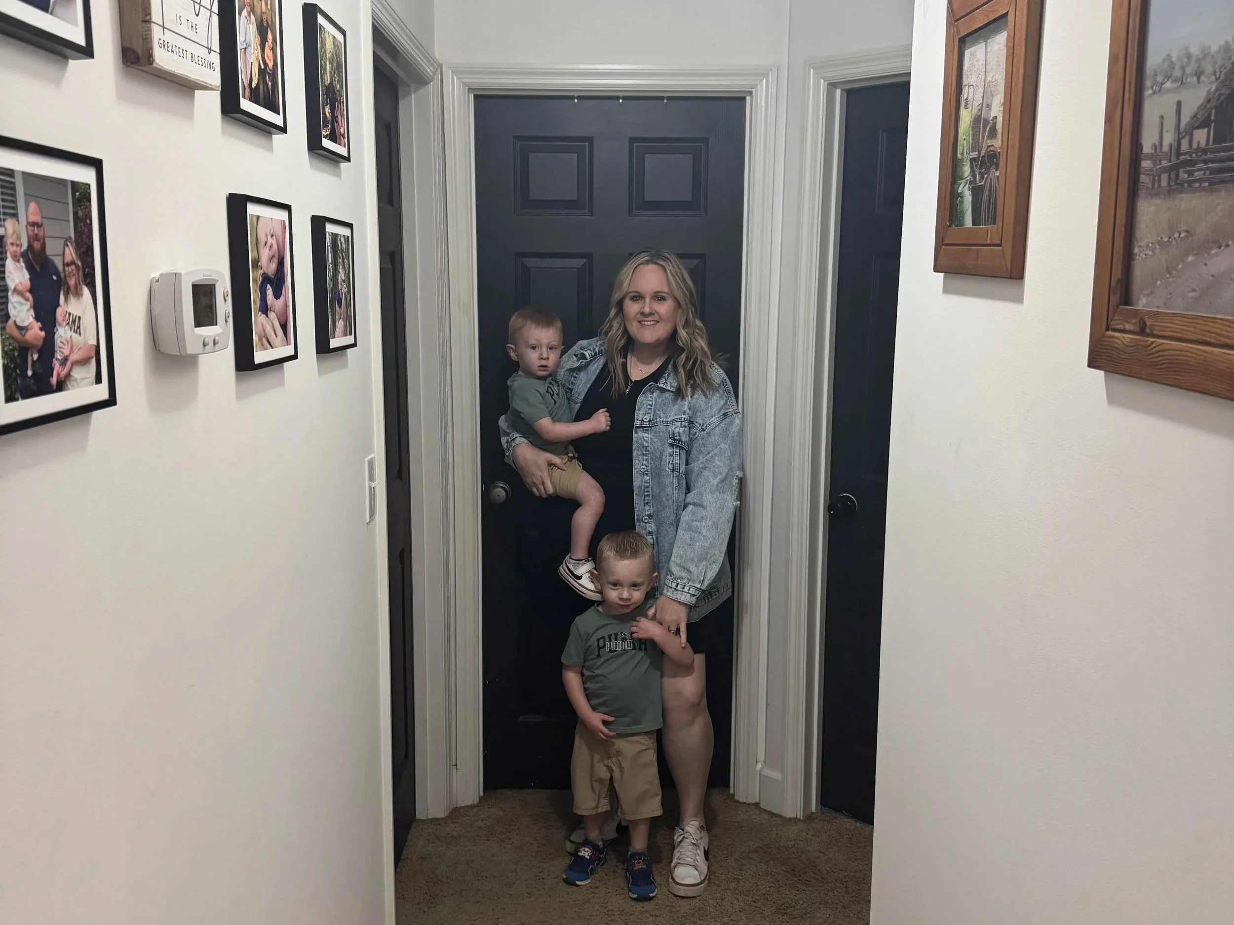 A woman holding a young boy in a hallway decorated with family photos and framed pictures on the walls.