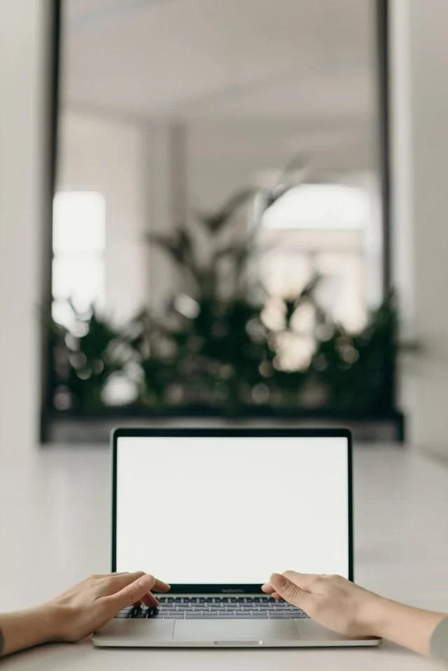 Person using a laptop in front of a large mirror with plants reflected in it.