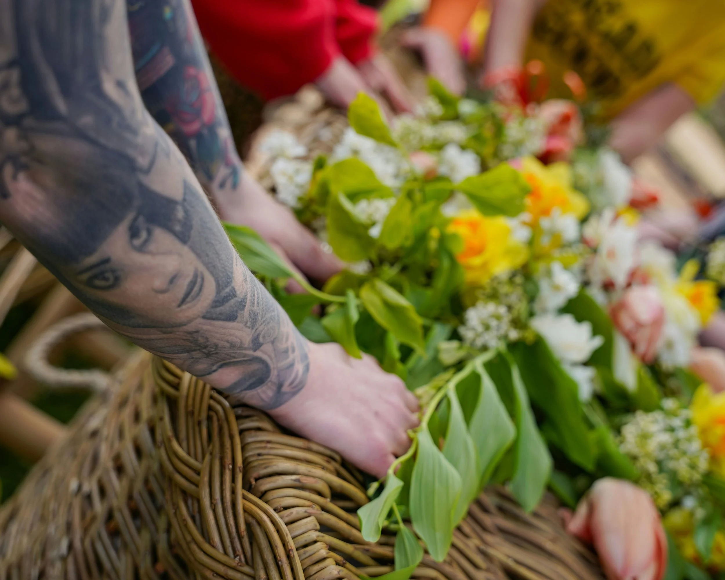 People planting flowers in a garden, with a wicker basket visible in the foreground and greenery in the background.