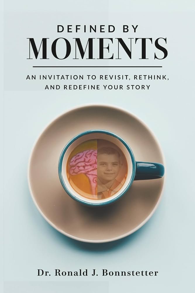 Book cover titled "Defined by Moments" by Dr. Ronald J. Bonnstetter, featuring a coffee cup with a brain and a person's face reflected in the liquid.