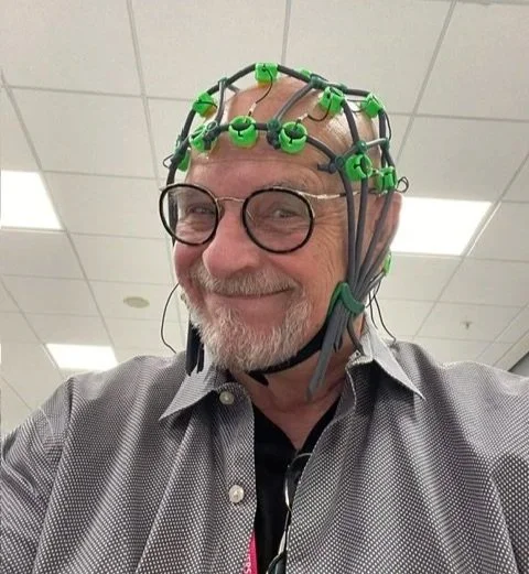 A man smiling wearing a cap with multiple green and black EEG electrodes attached to his head