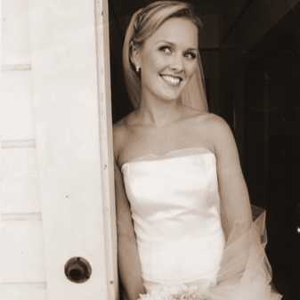 A woman in a strapless wedding dress smiling and peeking out from behind a door.