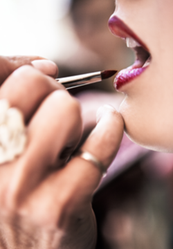Close-up of a woman getting her lips painted with lipstick by a makeup artist