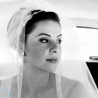 Black and white photo of a bride with a veil, sitting inside a vehicle, looking out the window.