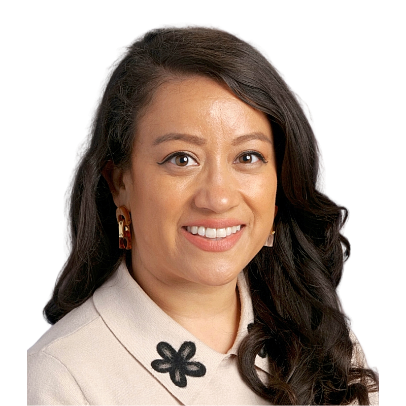 A woman with long dark hair, smiling, wearing a beige top with floral embellishments and gold earrings, against a black background.