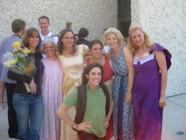 Group of women dressed in colorful outfits, with one woman wearing a tiara, posing outside for a photo.