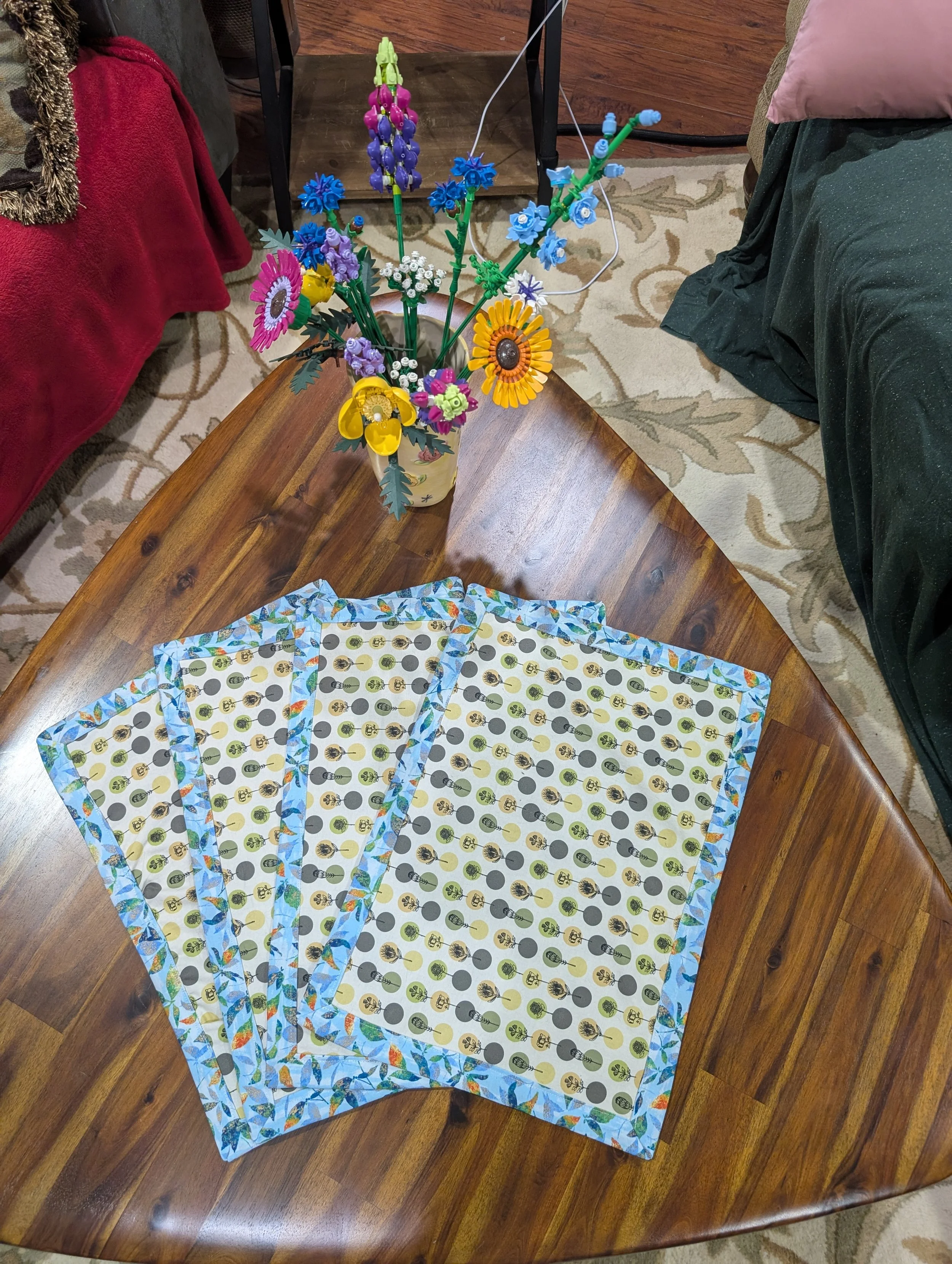 Four placemats with a cream and green floral pattern, and a light blue border, in a playing card spread.