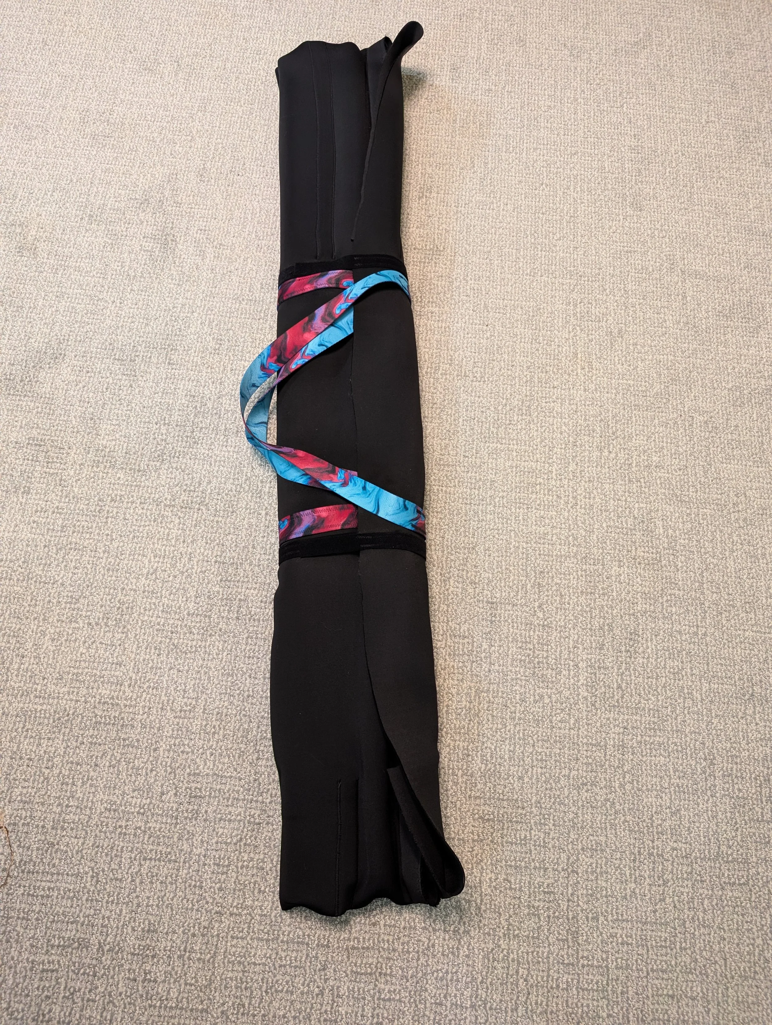 A black carrying case with a colorful ribbon around it, lying on a beige carpet.