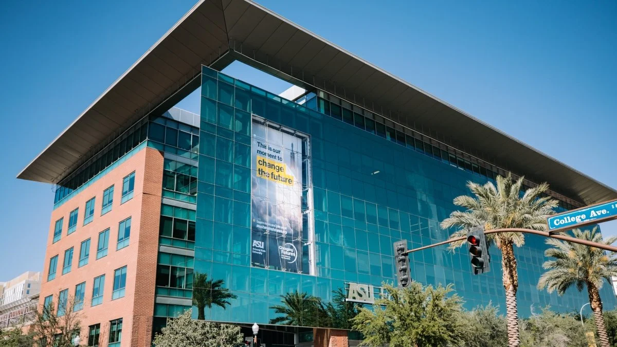 Modern office building with glass facade, palm trees, and a street sign for College Ave. The building has a large banner that reads "This is our moment to change the future."