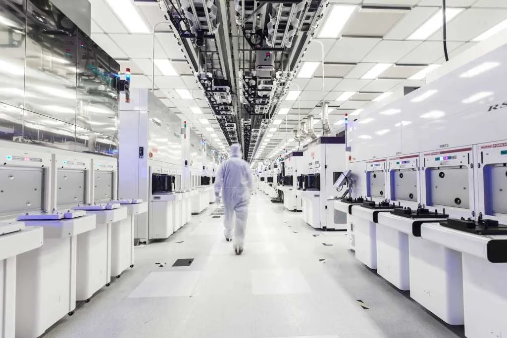 A person walking through a highly advanced, sterile laboratory or factory filled with rows of white machines and testing equipment.
