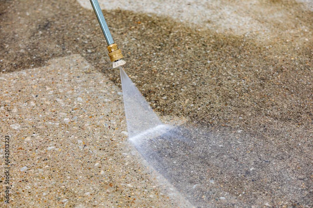 A pressure washer nozzle spraying water on a sandy surface.