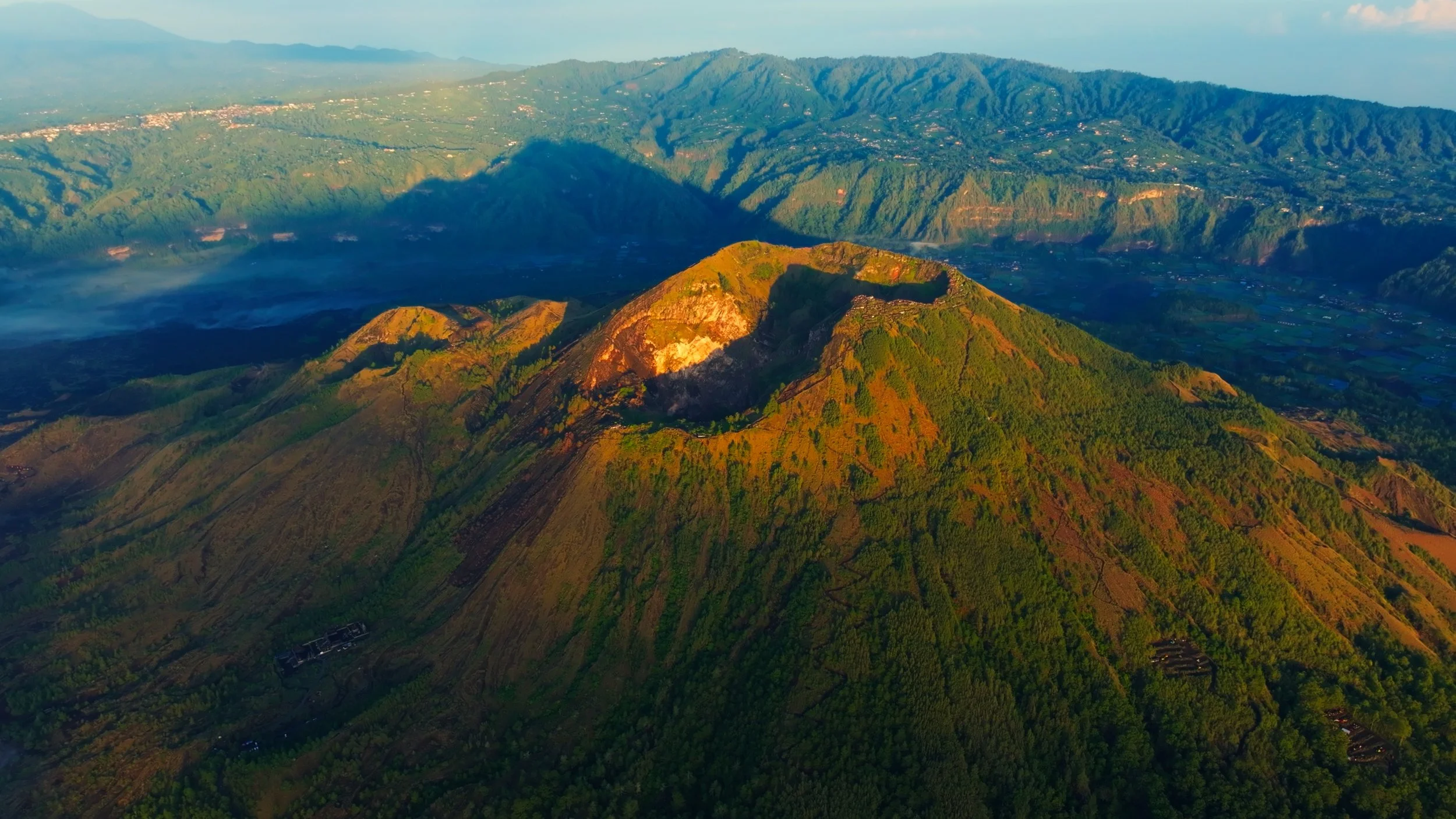 Paisaje de montañas verdes con cumbres y laderas cubiertas de vegetación, al amanecer o atardecer.